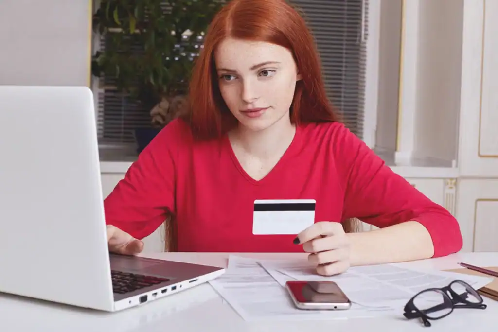 Person holding a bank card while entering payment details on a laptop, illustrating online payment verification - Zeevou